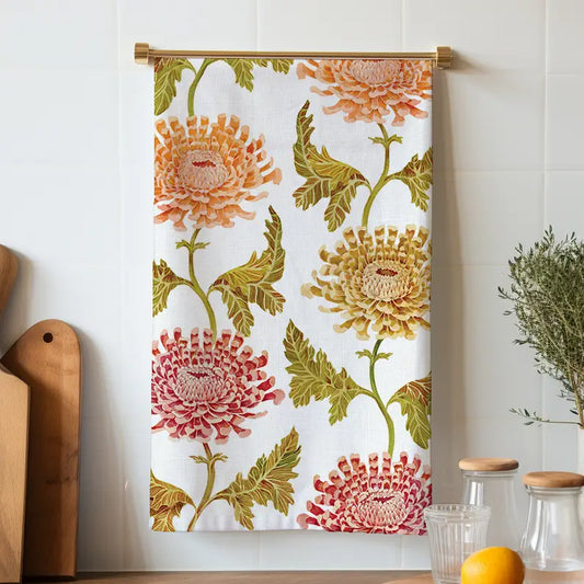 White chrysanthemum tea towel hanging from a brass rod, with peach, red, and yellow-green flowers and olive leaves.